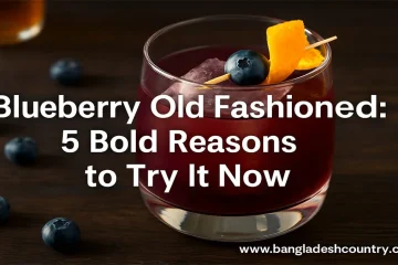 A Blueberry Old Fashioned cocktail in a rocks glass with ice, garnished with a fresh blueberry on a skewer and an orange peel. Several loose blueberries are scattered on a dark wooden table around the glass. The image prominently features the text overlay: 'Blueberry Old Fashioned: 5 Bold Reasons to Try It Now' and 'www.bangladeshcountry.com'.