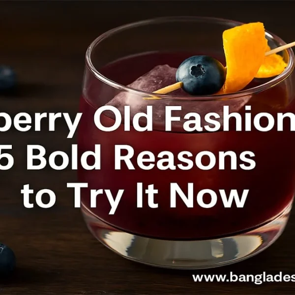A Blueberry Old Fashioned cocktail in a rocks glass with ice, garnished with a fresh blueberry on a skewer and an orange peel. Several loose blueberries are scattered on a dark wooden table around the glass. The image prominently features the text overlay: 'Blueberry Old Fashioned: 5 Bold Reasons to Try It Now' and 'www.bangladeshcountry.com'.