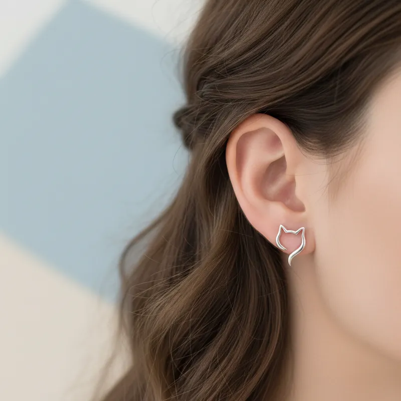 A close-up shot of a woman's ear adorned with a delicate sterling silver cat silhouette stud earring, with soft focus on her hair and a modern, clean