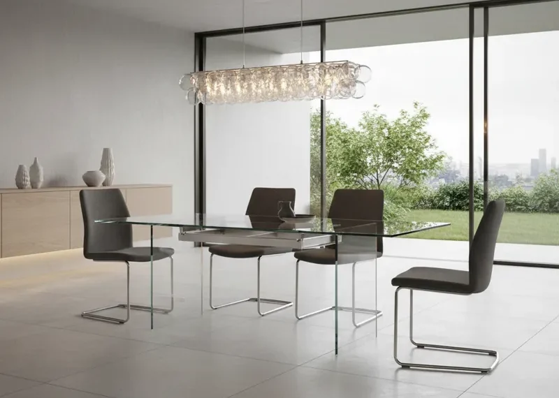 Modern extendable glass dining room table with a clear top and polished metal base, showcasing its sleek design and versatility for dining spaces.