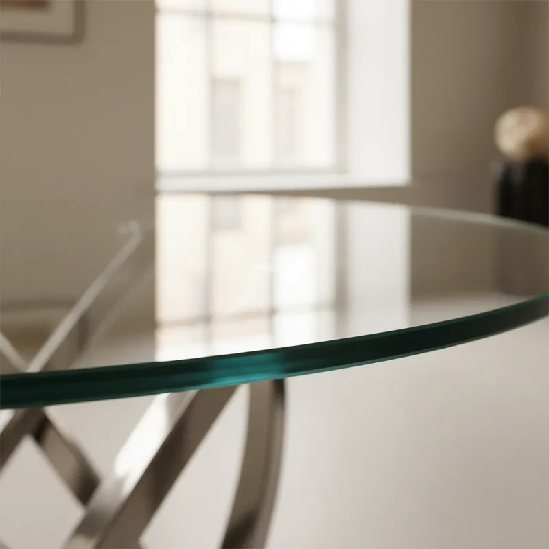 A close-up shot of a thick, tempered glass tabletop on an oval dining table, showing the smooth, polished edge. The focus highlights the quality of th
