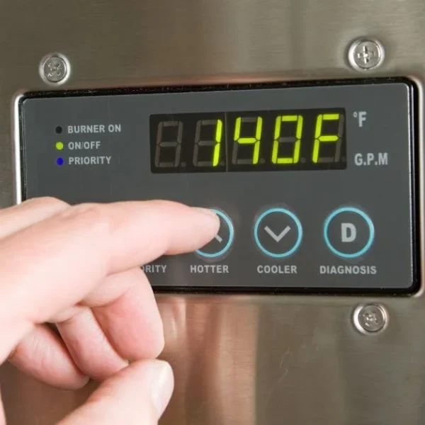 Close-up of a hand pressing the 'HOTTER' button on a Rheem tankless water heater's digital control panel, displaying a temperature of 140°F. The panel also shows indicators for 'BURNER ON', 'ON/OFF', and 'PRIORITY', along with 'G.P.M' and 'COOLER' and 'DIAGNOSIS' buttons.