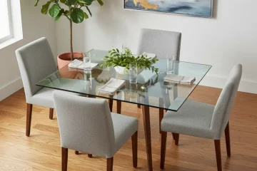 Modern square glass dining room table with a clear top and polished metal base, showcasing its sleek and minimalist design in a contemporary dining space.