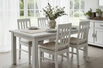 A stylish whitewash dining table set featuring a rectangular solid wood table and six matching chairs with a distressed finish, set in a bright, modern farmhouse dining room.